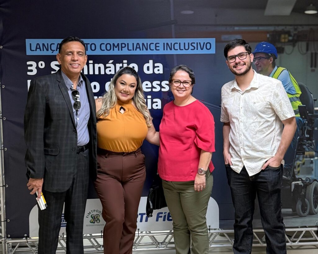 Quatro pessoas estão em pé, sorrindo, em frente a um painel azul com o texto “3° Seminário da Inclusão da Pessoa com Deficiência nas Indústrias”. Da esquerda para a direita: Trajano Figueiredo, Presidente do FIMTPODER, veste terno escuro e camisa clara; Andreia Kran, Gerente de Departamento Pessoal e Presidente do Comitê Novo Olhar para Diversidade na ENGESP, usa blusa mostarda e calça marrom; Eleides Souza, Presidente da APOIA, veste blusa vermelha e calça verde; e Lucas Torres, Analista de Departamento Pessoal e Secretário do Comitê Novo Olhar para Diversidade na ENGESP, usa camisa branca e calça jeans escura. O grupo posa em ambiente interno, sob iluminação clara, transmitindo alegria e engajamento com o tema da inclusão.
